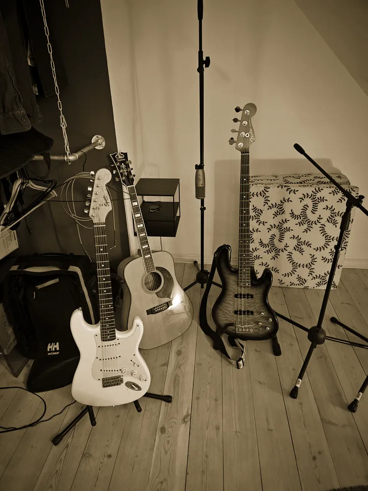 Electric guitars, bass and an acoustic on stands beside a mic stand